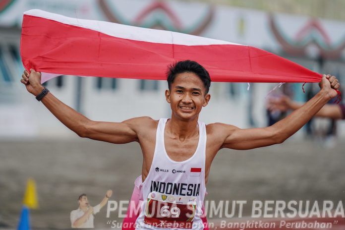Teks foto : Pelari Indonesia Yad Hafizudin berlari mengibarkan bendera Merah Putih usai memenangkan lomba lari kategori pria 1.500 meter U 20 pada event kejuaraan Atletik Asia Tenggara U-18 & U-20 di Stadion Madya Atletik Kawasan Sport Centre Sumut, Kabupaten Deliserdang, Provinsi Sumatera Utara, Sabtu (15/11/2025). Pelari asal Lombok Timur menjadi penyumbang medali emas pertama pada event ini dengan catatan waktu 3:56.94. (Foto : Ist)